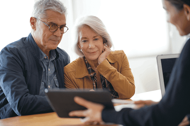 Man & woman sitting with someone reviewing something on a tablet