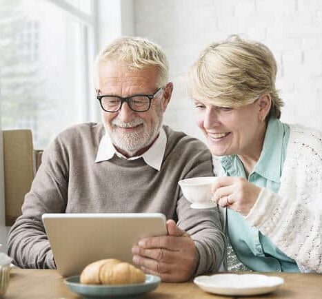Man & woman sitting at a table looking on their tablet