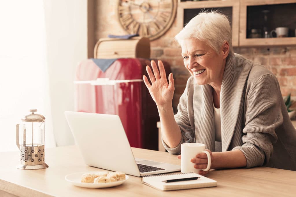 Woman sitting at table with coffee face timing on her computer