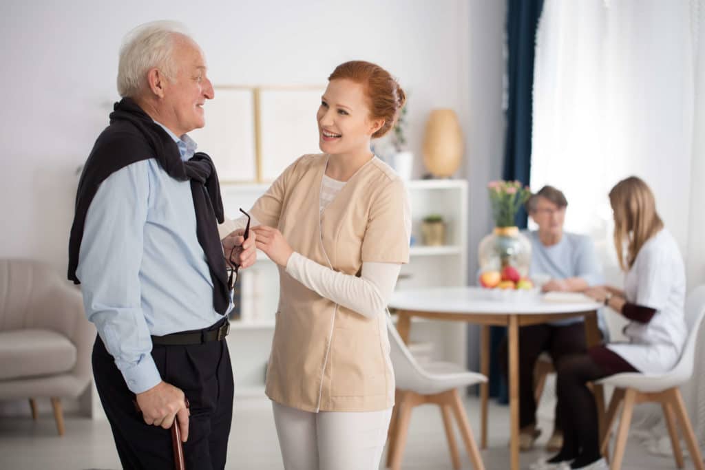 Two women sitting at a table while a nurse assist a male resident