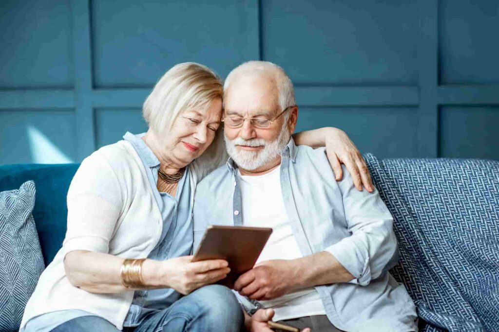 Man & woman sitting on blue couch smiling looking on their tablet