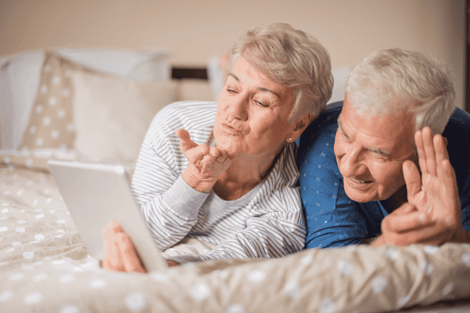 Man & woman laying across their bed looking on their tablet