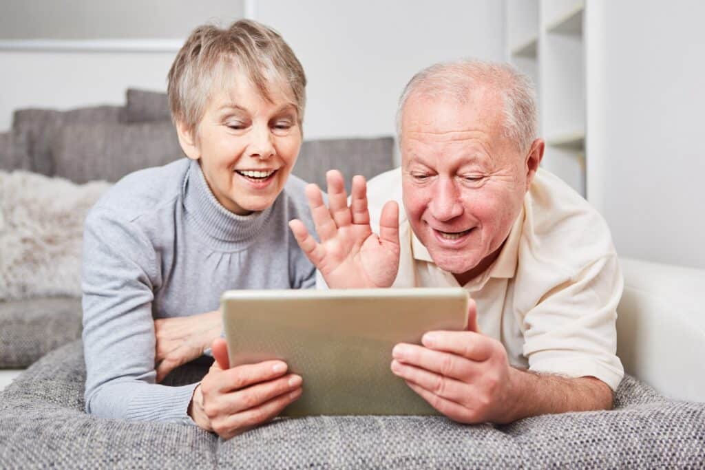 Man & woman laying across their couch looking on their tablet