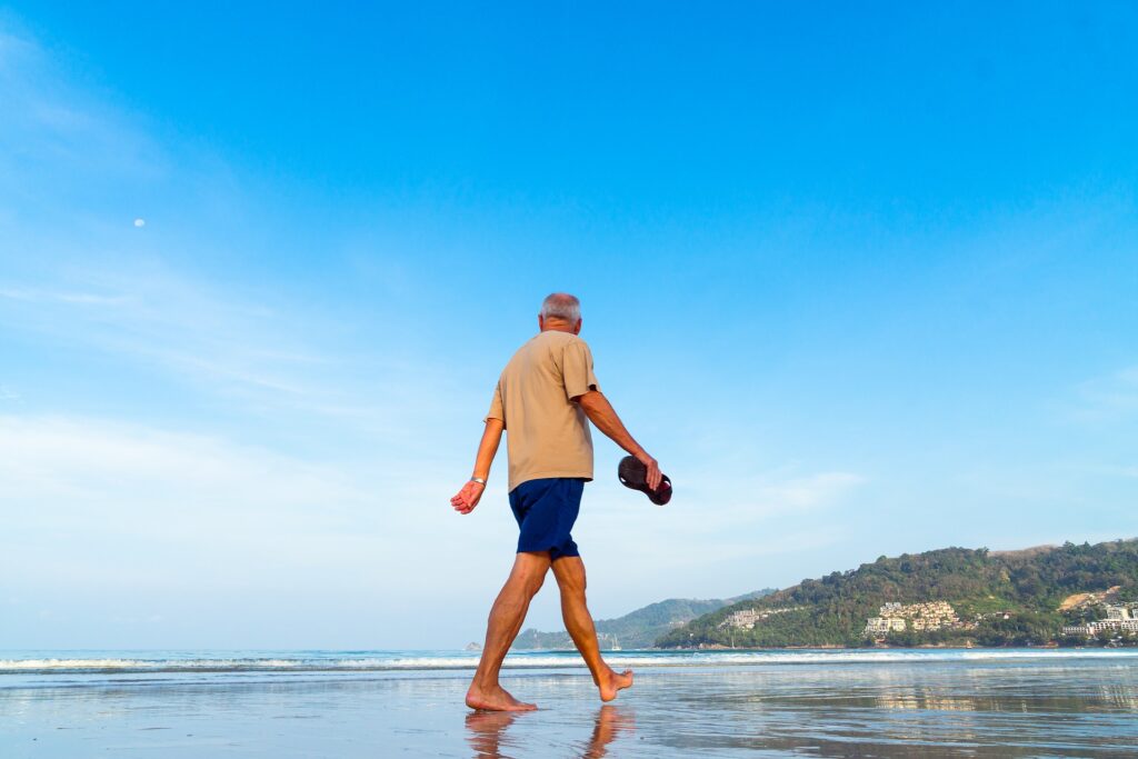 Man walking across the beach barefoot holding his shoes