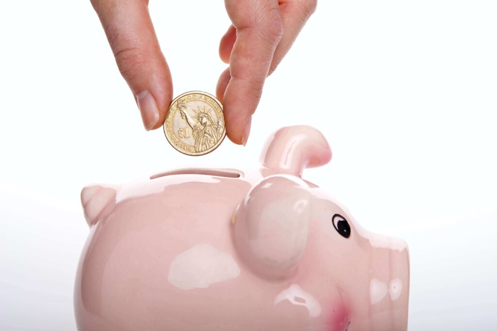 Hand adding a coin to a pink piggy bank