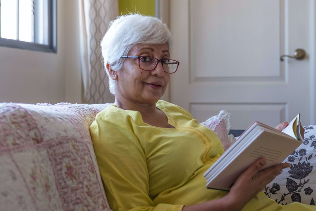 Woman in yellow shirt sitting on the couch reading a book