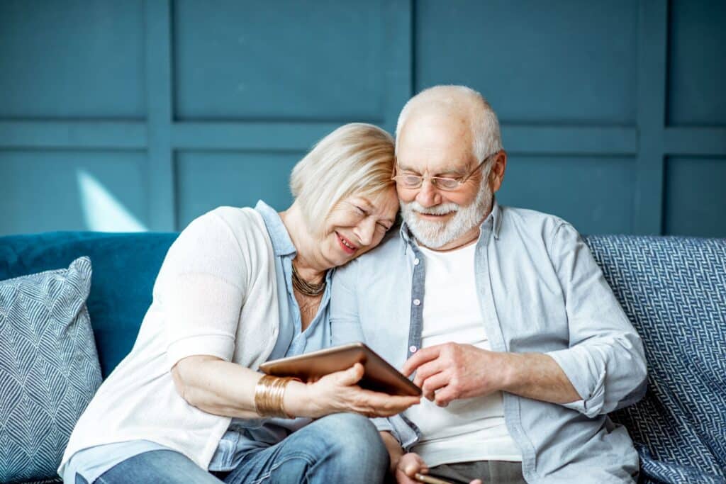 Man & woman sitting on blue couch smiling looking on their tablet