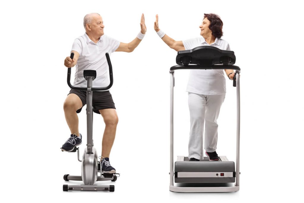 Man on exercise bike and woman on treadmill giving high five