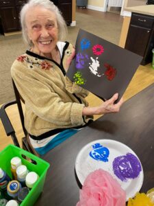 Woman holding up her painting while sitting at Traditions of Spring Hill