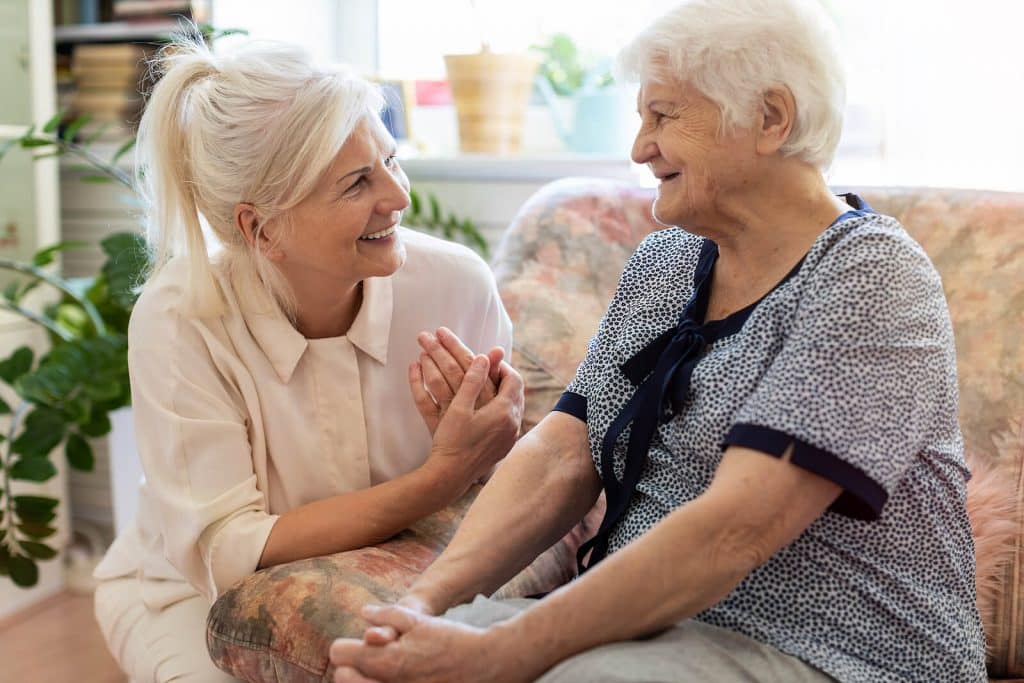 Woman kneeling talking to woman sitting in chair