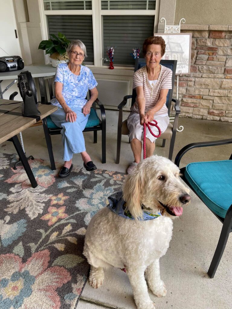 Women sitting while smiling with a dog on a leash
