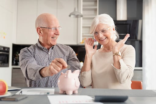 Photo of a man & woman adding a coin into their pink piggy bank