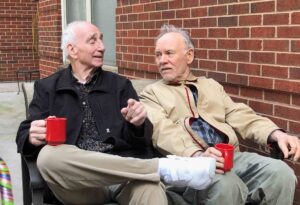 Photo of two men sitting on a bench outdoors enjoying a cup of coffee