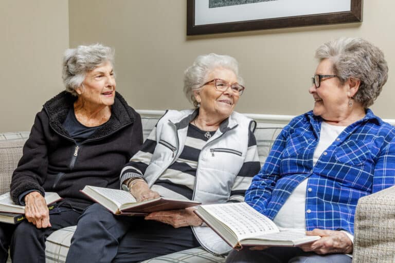 Three women sitting on a couch indoors discussing a book