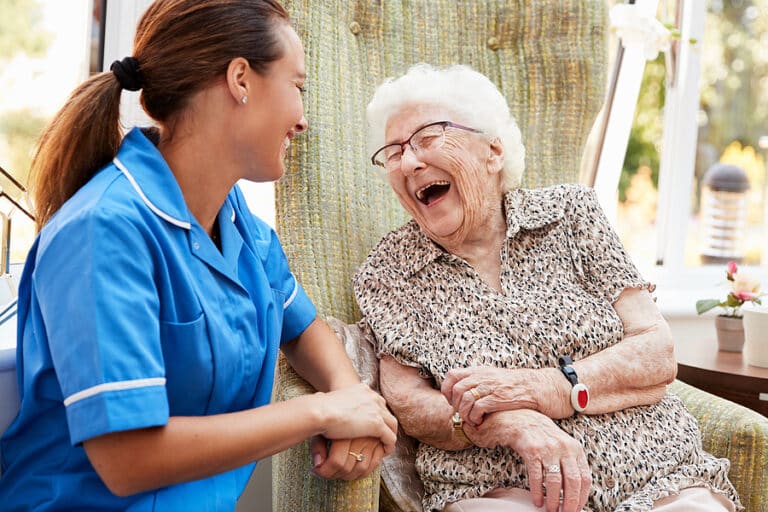 Senior Woman Sitting In Chair And Talking With Nurse In Senior Living Home