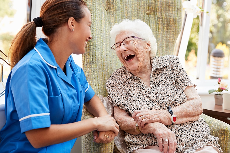 Senior Woman Sitting In Chair And Talking With Nurse In Senior Living Home