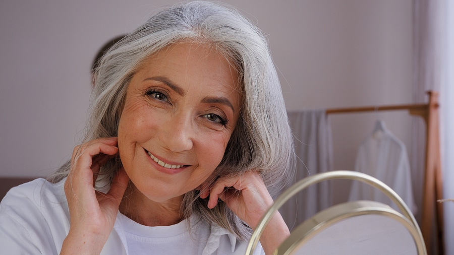 Older woman looking in mirror smiling, reflecting aging gracefully.