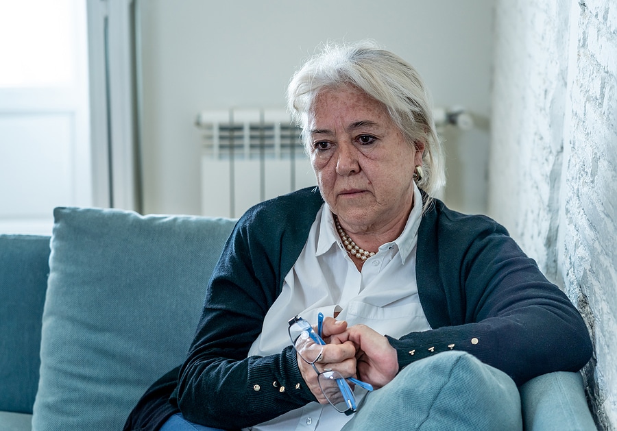 Older woman sitting alone on couch looking worried or lonely