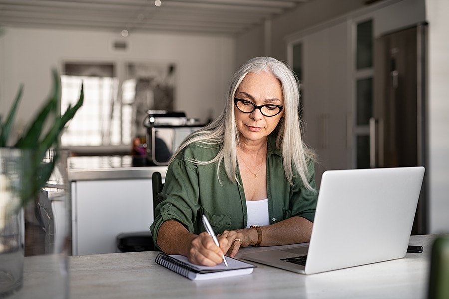 Senior Woman researching senior living questions on her laptop and taking notes.