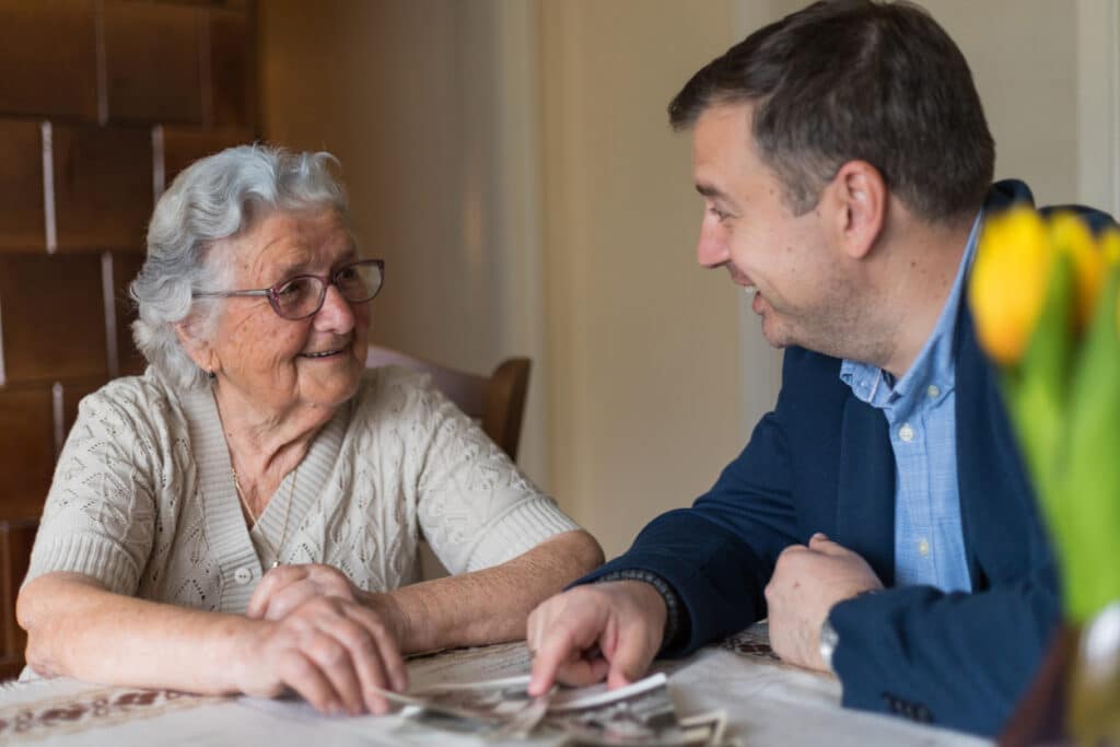 Senior woman with her adult grandson are looking old photos and remember the old memories.Man enjoys the company of his grandmother and spending wonderful time with her.