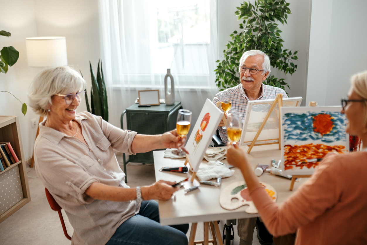 Group of senior residents, including one man and two women, enjoying a relaxing painting session together. Creative activity fostering community and well-being in a warm care environment.