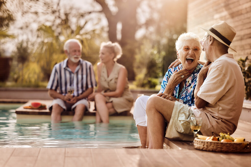 Cheerful senior couple talking by the pool during social gathering in summer day at the backyard.