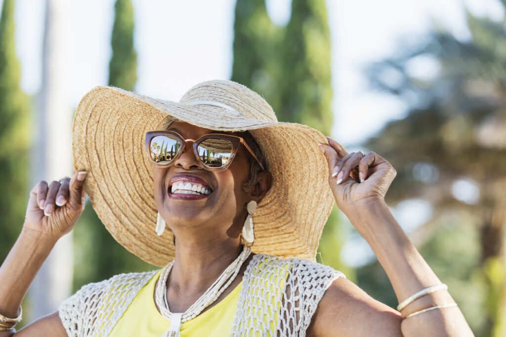 Senior woman smiling, wearing an oversized sun hat and sunglasses