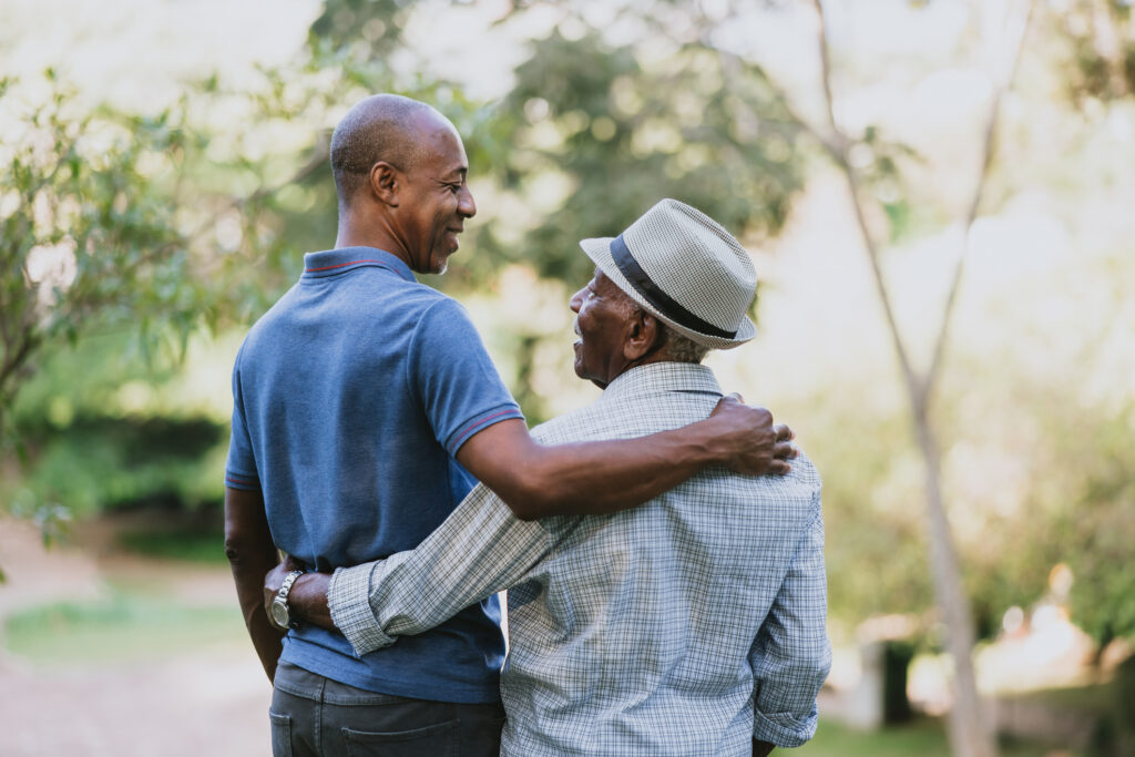 Senior man standing with adult son, smiling at each other